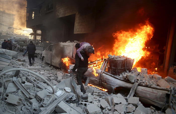 ATTENTION EDITORS - VISUAL COVERAGE OF SCENES OF DEATH AND INJURYA man carries an injured child amidst rubble near a burning vehicle in a site damaged from what activists said was shelling by forces loyal to Syria's President Bashar al-Assad in the town of Douma, eastern Ghouta in Damascus, Syria December 30, 2015. REUTERS/Bassam Khabieh - RTX20JO0